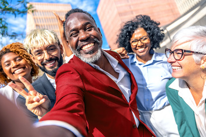 Orang daripada pelbagai peringkat umur, bangsa dan jantina tersenyum lebar di luar bangunan